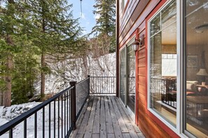 Wooden deck with black railings overlooking snowy trees outside sliding glass doors. - Elkhorn Lodge | 3BR Mountain Condo |  Sleeps 8 (Sandpoint)