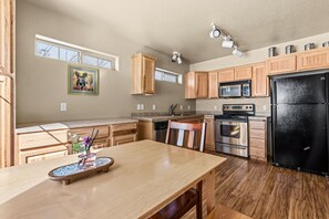 A modern kitchen with wooden cabinets, a black refrigerator, stainless steel appliances, and a dining area with a wooden table and chairs. - Elkhorn Lodge | 3BR Mountain Condo |  Sleeps 8 (Sandpoint)