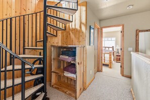 Een houten interieur met een spiraaltrap, een inbouwkast met opgevouwen handdoeken en uitzicht op een slaapkamer met een bed en nachtkastje.