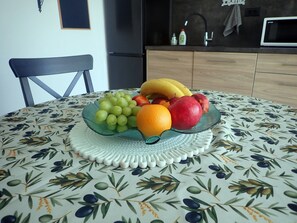 Uma mesa de jantar com uma tigela de frutas contendo uvas, uma laranja e uma romã.