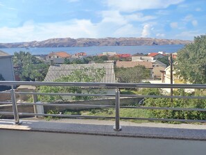 A balcony with a metal railing overlooking a residential area with houses and a body of water in the distance. - Holiday home in Karlobag with seaview (Karlobag)