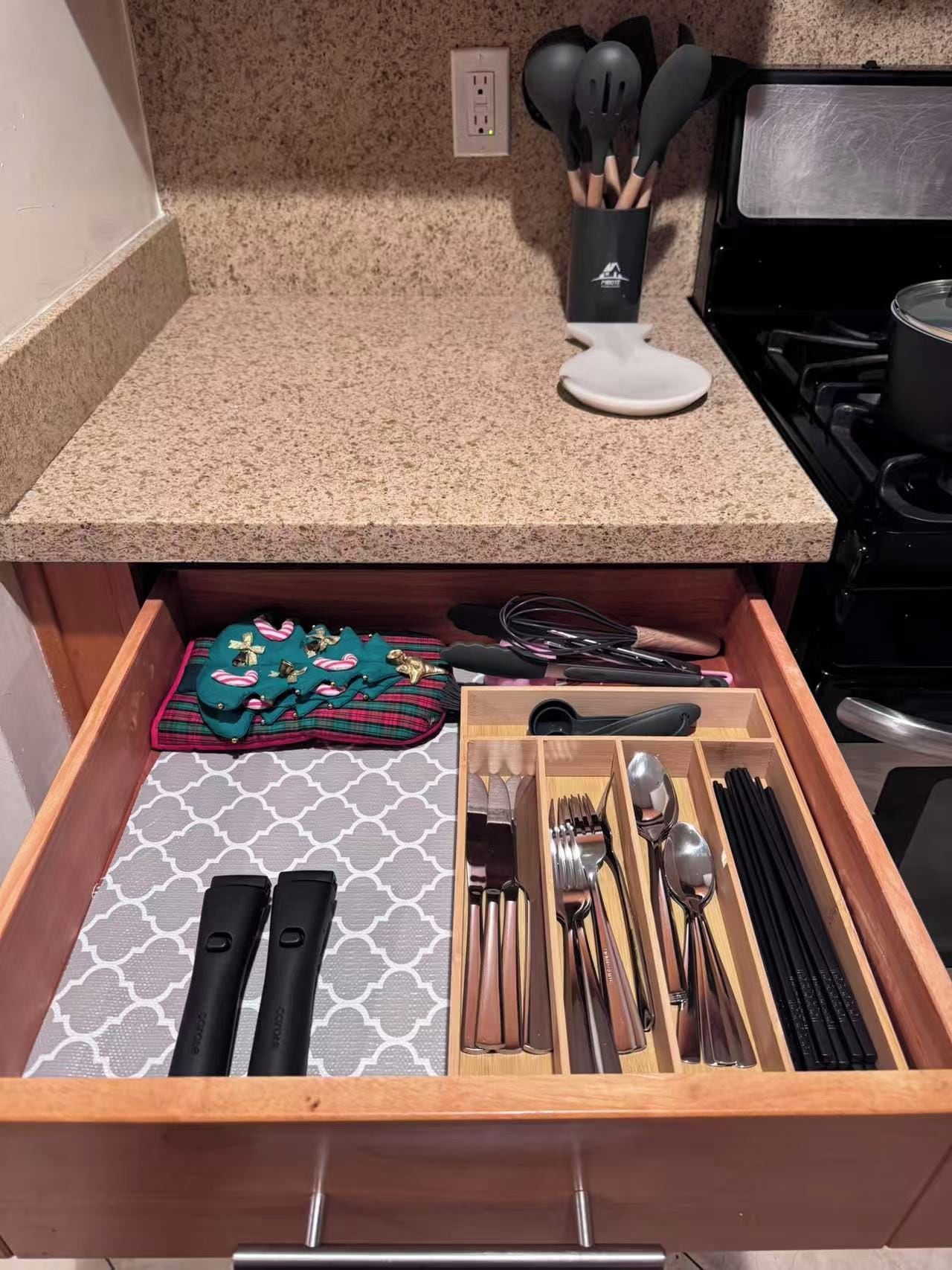 A kitchen with a granite countertop, a stove, and a drawer organizer with utensils.