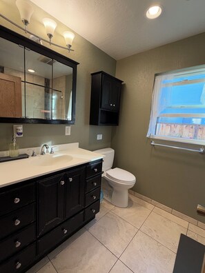 Een badkamer met een wit wastafelmeubel, zwarte kastjes, een toilet en een raam met uitzicht.