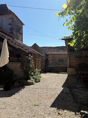 A courtyard with stone buildings, a gravel path, and a wooden table. - Vacation rental in a converted barn that sleeps up to 10 people (Villeneuve)