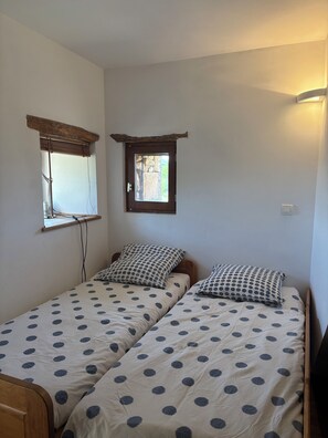 A bedroom with two single beds, each with a polka dot duvet, a window with a wooden frame, and a wall-mounted light fixture. - Vacation rental in a converted barn that sleeps up to 10 people (Villeneuve)