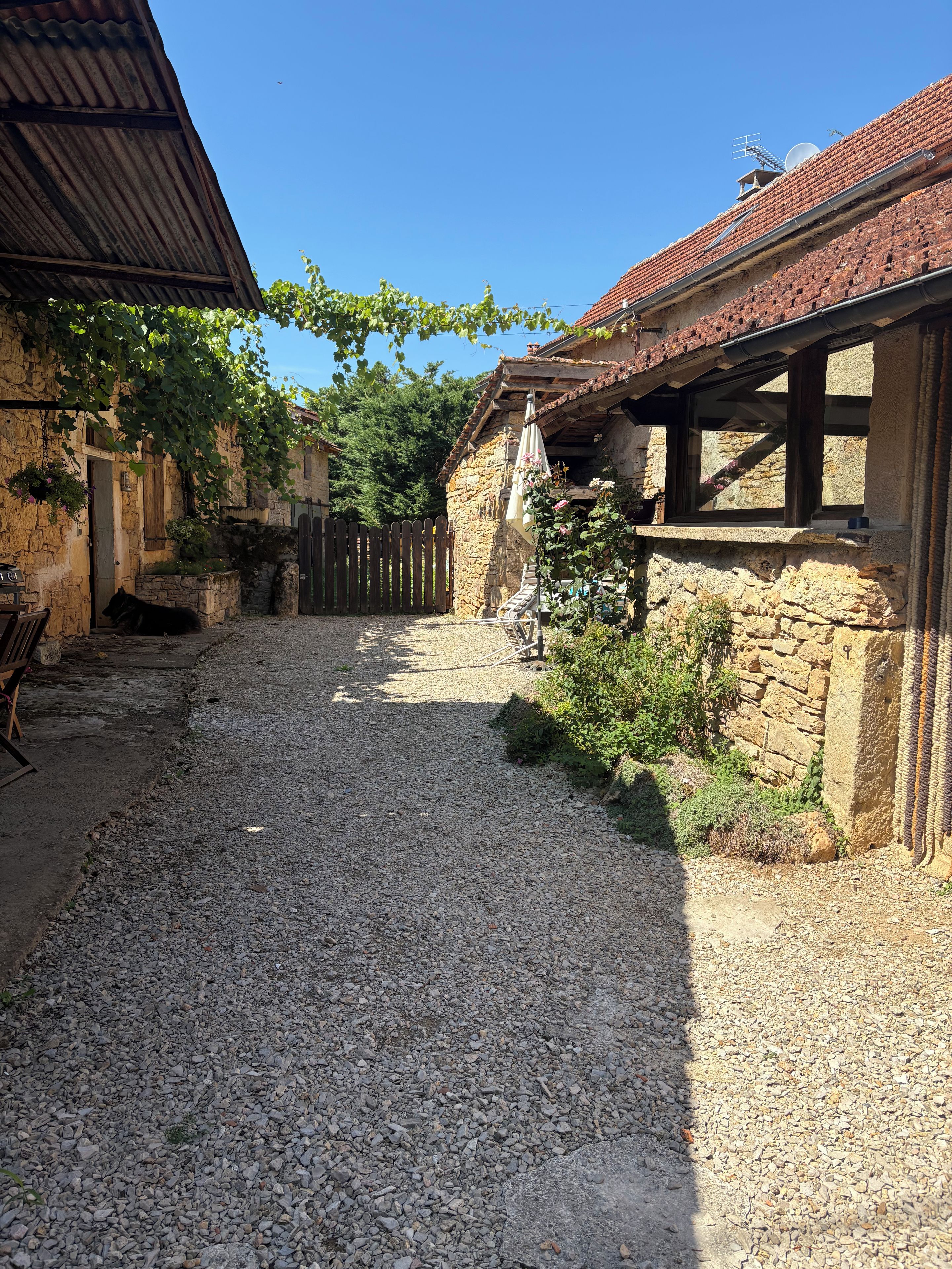 A rustic courtyard with a gravel path, stone walls, and a wooden fence.
