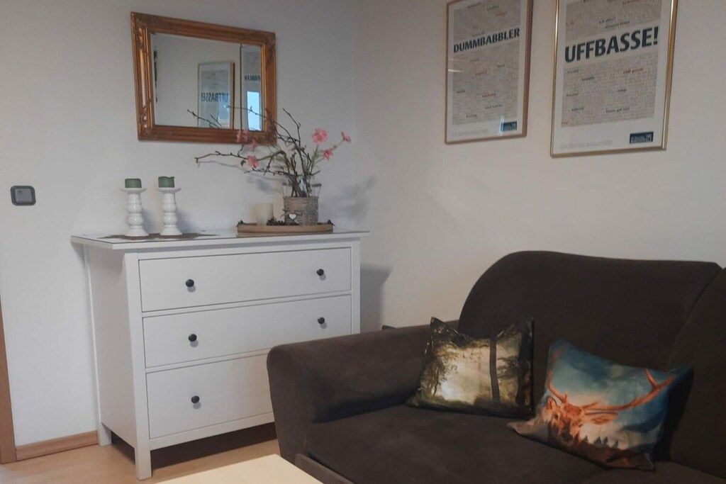 A room with a white dresser, a brown sofa, a mirror, and two framed certificates on the wall.
