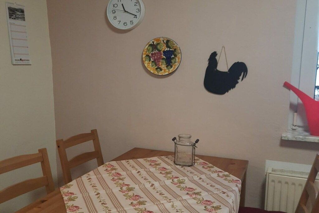 A dining area with a table, chairs, a clock, a decorative plate, and a rooster silhouette.