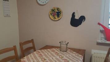 A dining area with a table, chairs, a clock, a decorative plate, and a rooster silhouette.