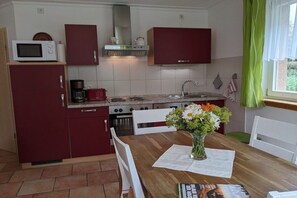 Eine kompakte Küche mit Mikrowelle, Herd und Spüle. Ein Esstisch steht dort, auf dem sich eine Blumenvase und eine Zeitschrift befinden.