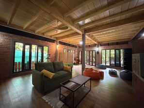 A spacious living area with a wooden ceiling, a green sofa, a coffee table, and a view through large windows.