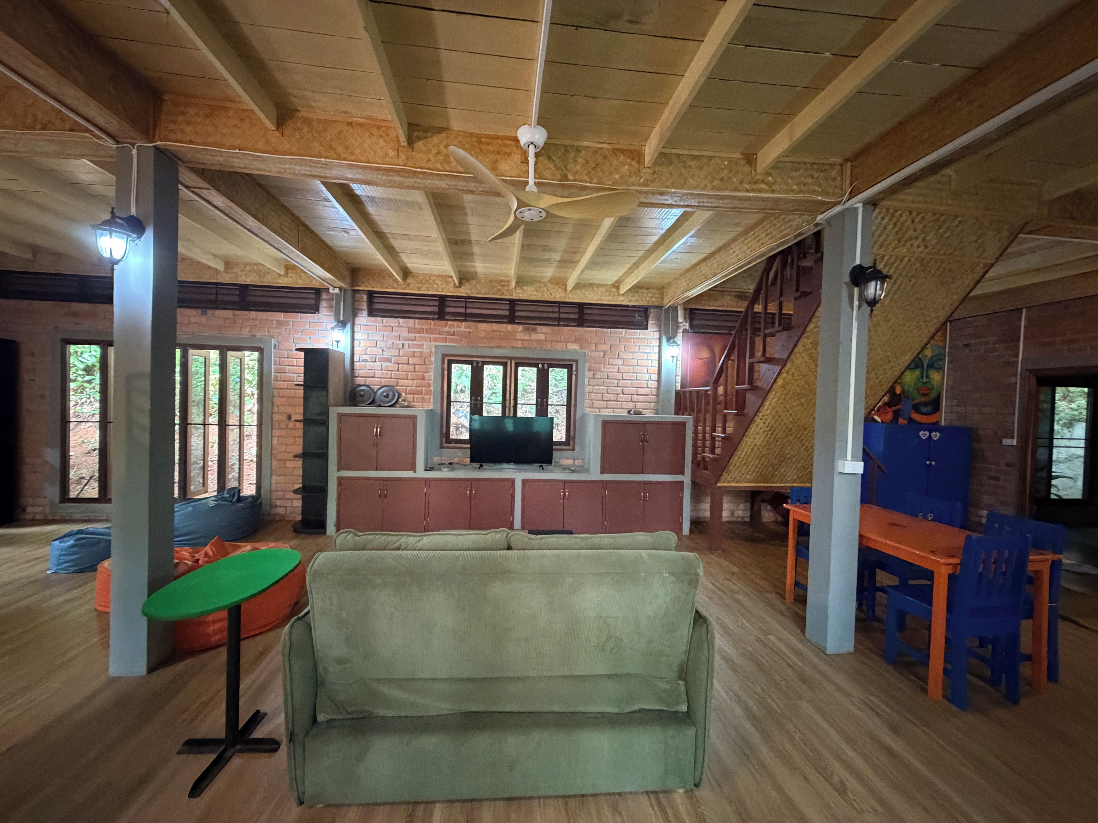 A spacious room with a high ceiling, wooden beams, a sofa, a television, and a staircase.