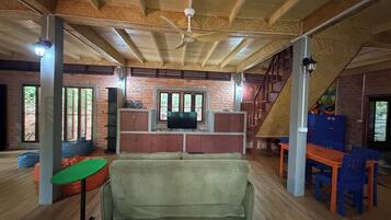 A spacious room with a high ceiling, wooden beams, a sofa, a television, and a staircase.