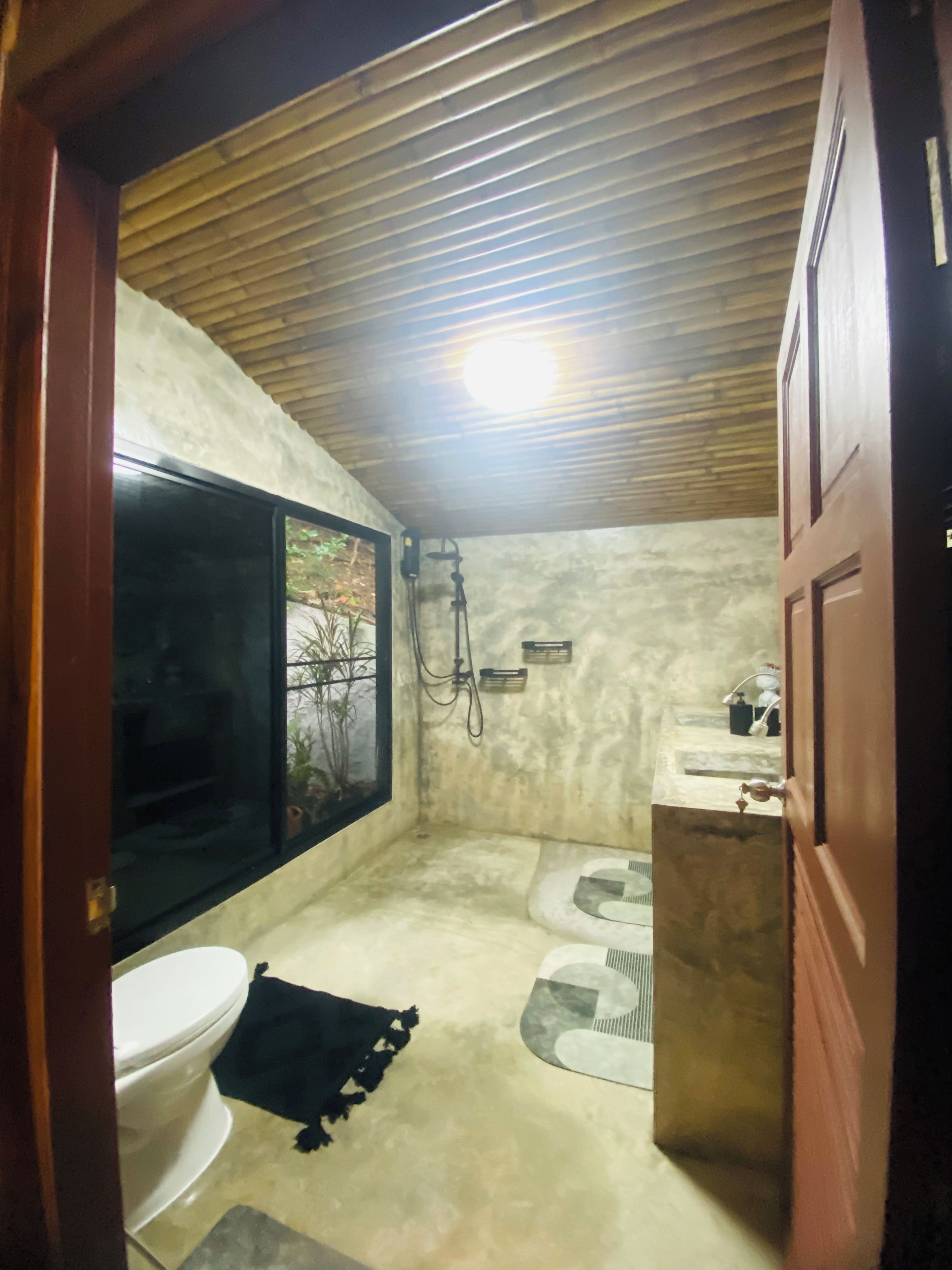 A compact bathroom with a toilet, bidet, and shower area, featuring a wooden ceiling and a window.