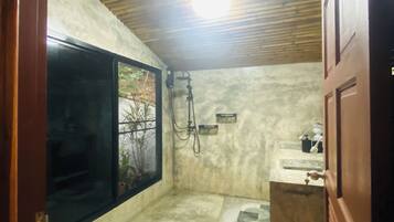 A compact bathroom with a toilet, bidet, and shower area, featuring a wooden ceiling and a window.