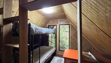 A dormitory room with bunk beds, a small table, and a window with a view of trees.