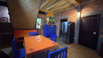 A kitchen with a brick wall, wooden ceiling beams, a refrigerator, and a table with chairs.