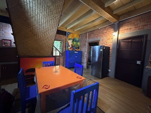 Eine Küche mit Backsteinwand, Holzbalkendecke, einem Kühlschrank und einem Tisch mit Stühlen.