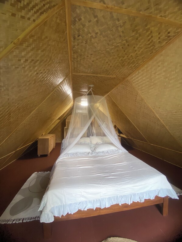 A single bed with a canopy in a room with sloped wooden walls.