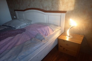 Un llit amb roba de llit estampada, una taula de nit de fusta amb una làmpada i una paret amb textura.