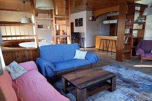 A cozy living area with a blue sofa, a wooden coffee table, and a pink sofa. There is a kitchen area with a bar and stools. - Holiday apartment with 3 bedrooms (Mühlingen)