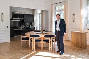 A modern kitchen with a central island, a dining area with a round table and chairs, and a large window providing natural light. - 200 m² Luxury on the Seine: Alma, George V, Montaigne (Paris)