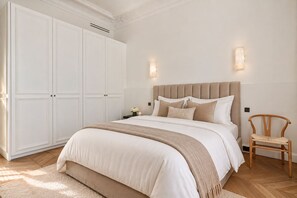 A bedroom with a large bed, a wooden chair, a wardrobe, and wall-mounted lighting. - 200 m² Luxury on the Seine: Alma, George V, Montaigne (Paris)