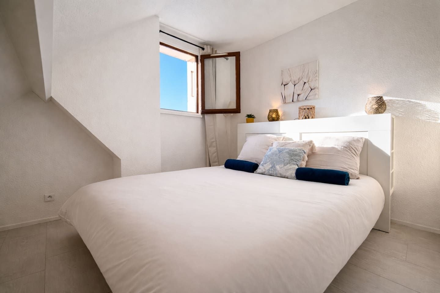 Une chambre à coucher avec un lit, une fenêtre et une œuvre d’art accrochée au mur.