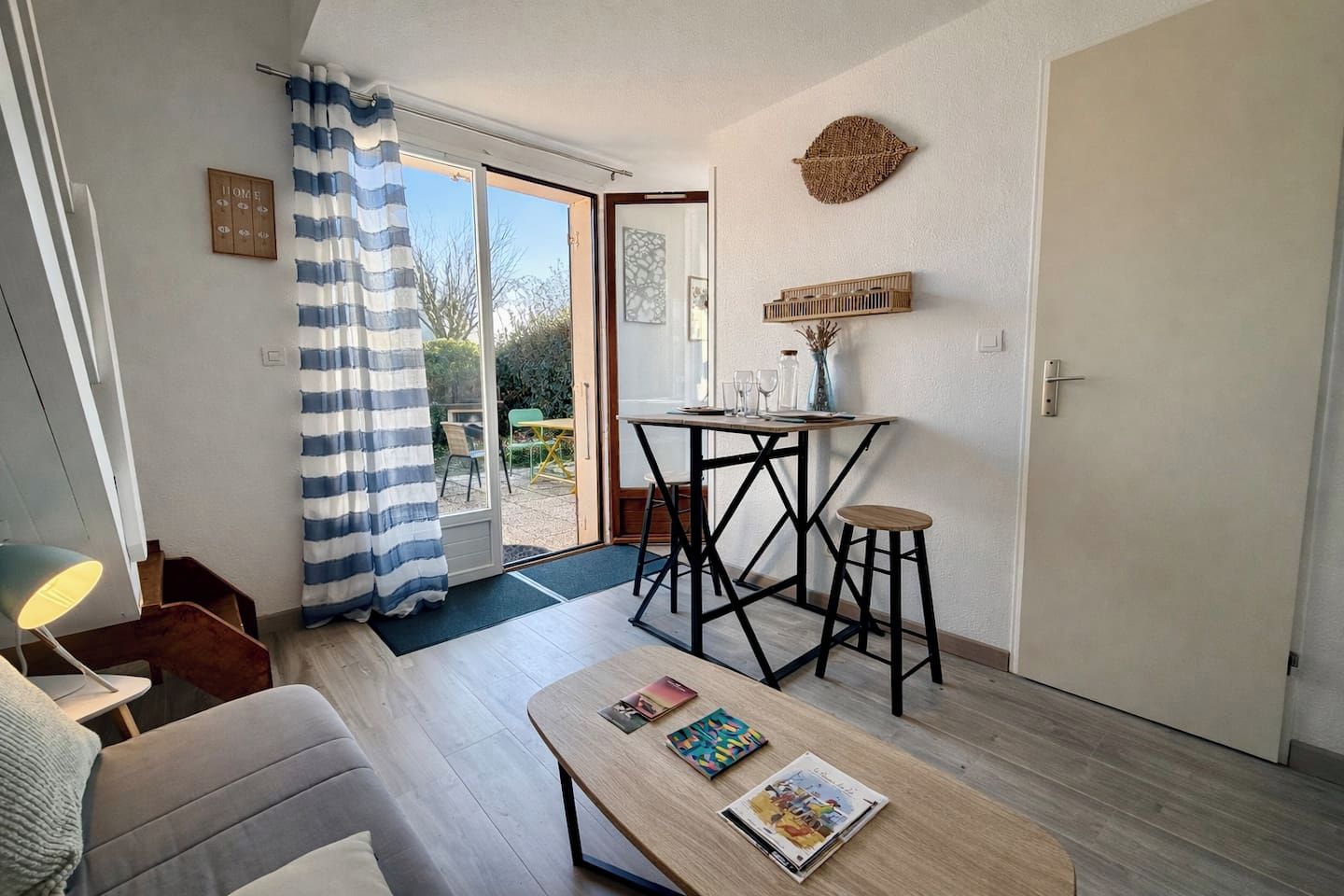 A cozy living area with a sofa, a coffee table with magazines, a dining table with chairs, a curtain, and a view of the outdoors.