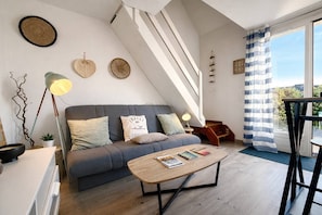 A modern loft-style living room with a grey sofa, a wooden coffee table, and a staircase leading to an upper level. - Fleur des Dunes - Beach - Pool - Garden (Erdeven)