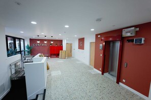 Passadís amb una taquilla d'informació, una paret vermella amb el rètol 'CENTRIC', un ascensor i un senyal de protecció contra incendis.