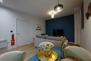 Ein modernes Wohnzimmer mit einer Couch, einem Esstisch mit Stühlen, einem Fernseher und einem Feuerlöscher.