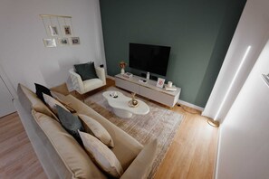 Ein modernes Wohnzimmer mit einer Couch, einem Couchtisch und einem Flachbildfernseher vor einer grünen Wand.