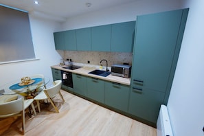 A compact kitchen with teal cabinets, a black sink, and a small countertop. - Modern City Centre Apartment| Moorfields| Sofa Bed (Merseyside)