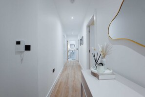 Un passadís modern amb terra de fusta, parets blanques i un taulell de recepció blanc amb un vas i espelmes.
