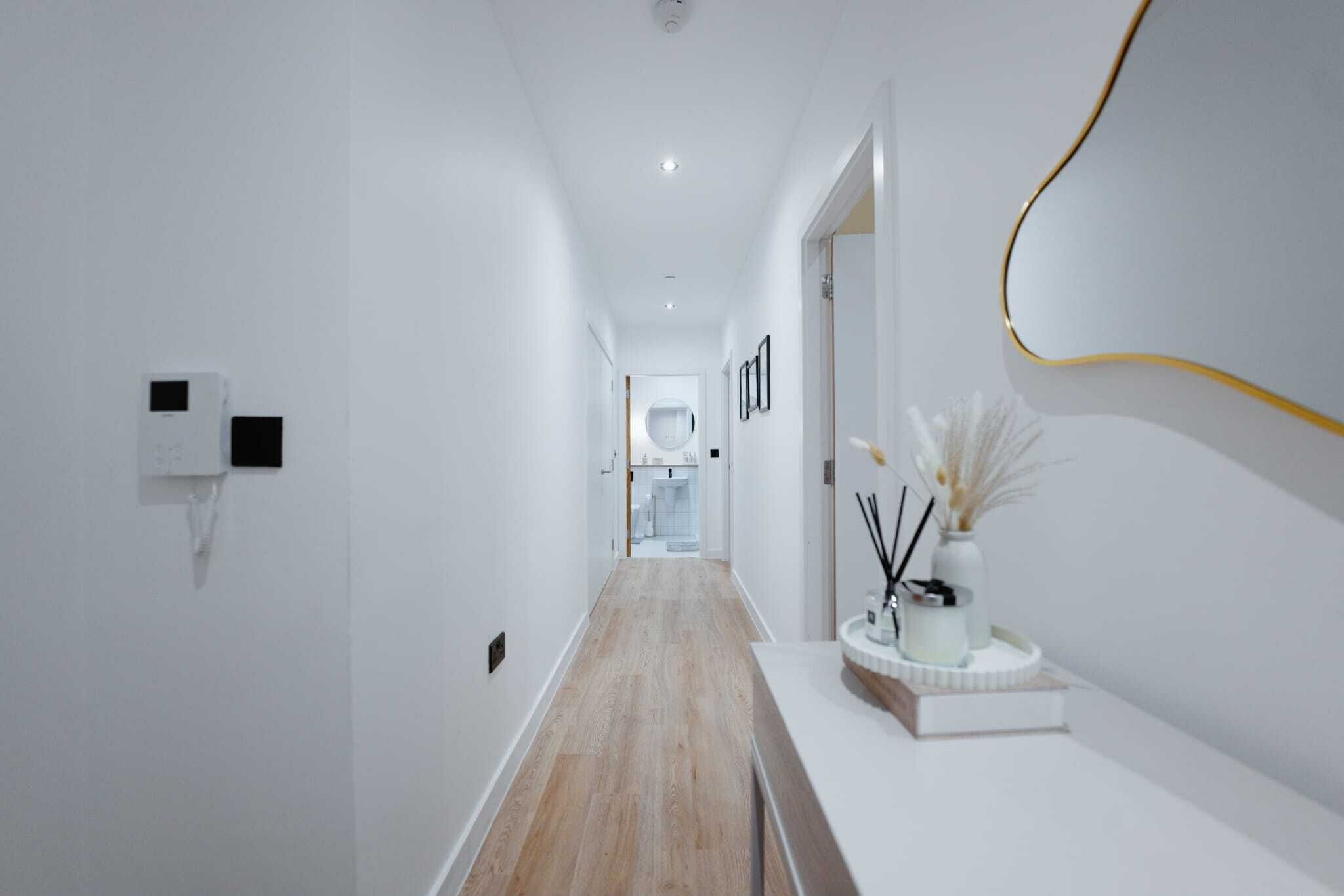 Un couloir moderne avec un plancher en bois, des murs blancs et un comptoir d’accueil blanc agrémenté d’un vase et de bougies.
