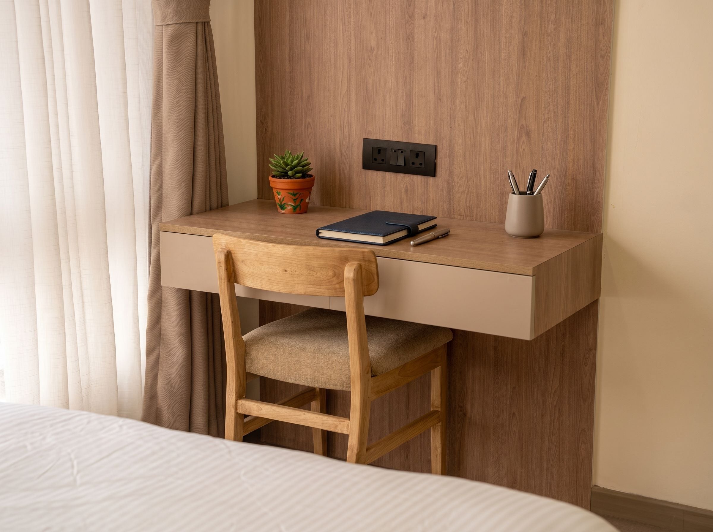 A compact workspace with a wooden desk, a chair, a potted plant, a notebook, and writing utensils.