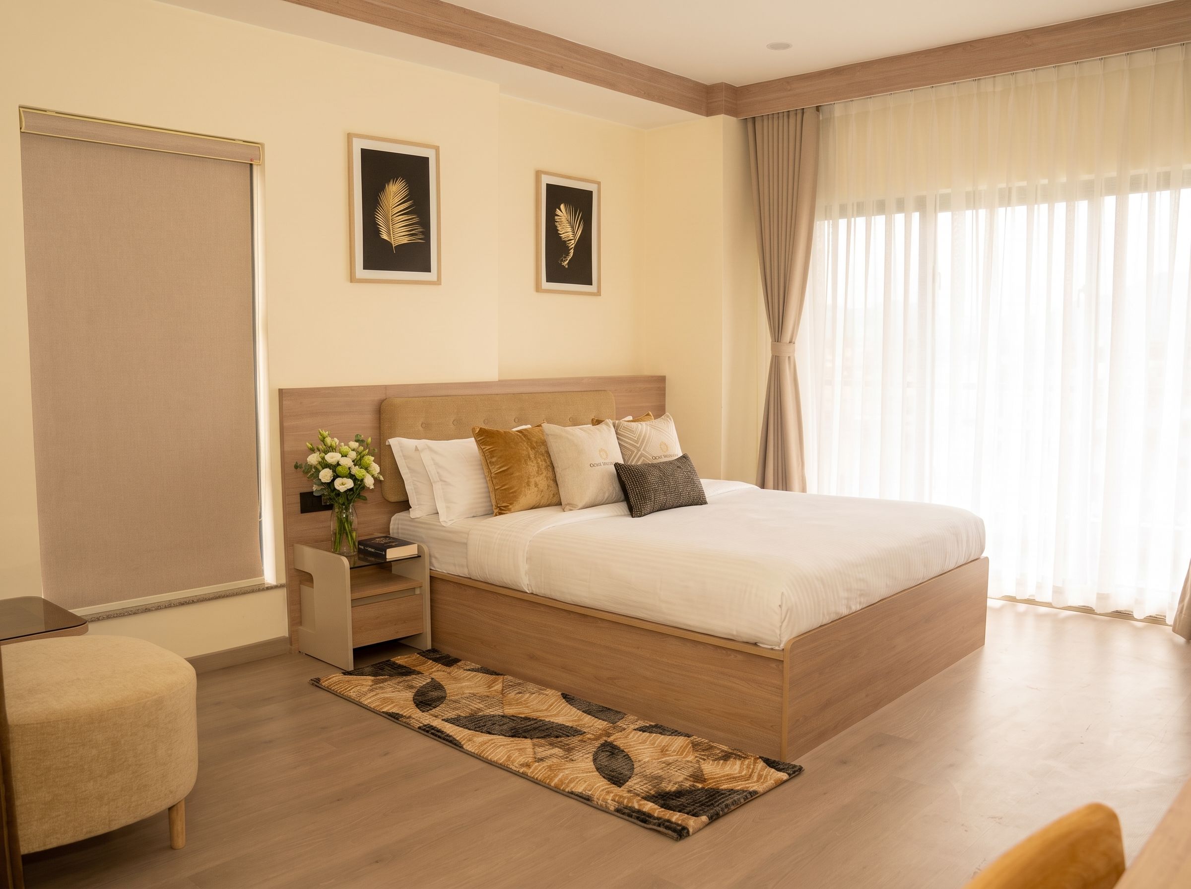 A hotel room with a bed, bedside tables, a nightstand, a chair, a window with curtains, and two framed wall art pieces.