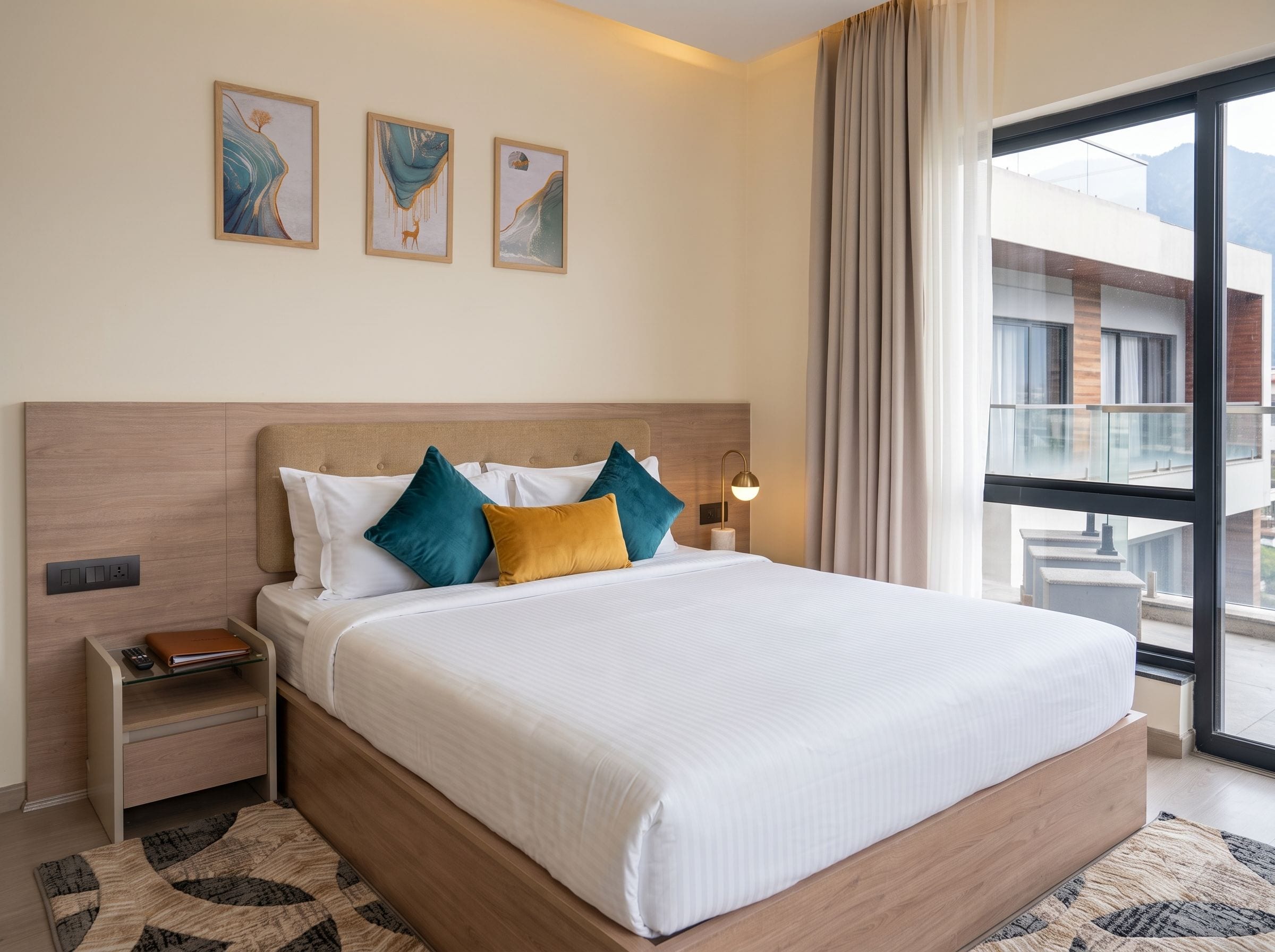 Ein Hotelzimmer mit einem großen Bett, einem Nachttisch, einer Lampe und Blick ins Freie.