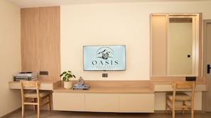 Una sala de estar moderna con un televisor de pared mostrando un logotipo, un banco de madera, una mesa pequeña con libros y una planta en maceta.
