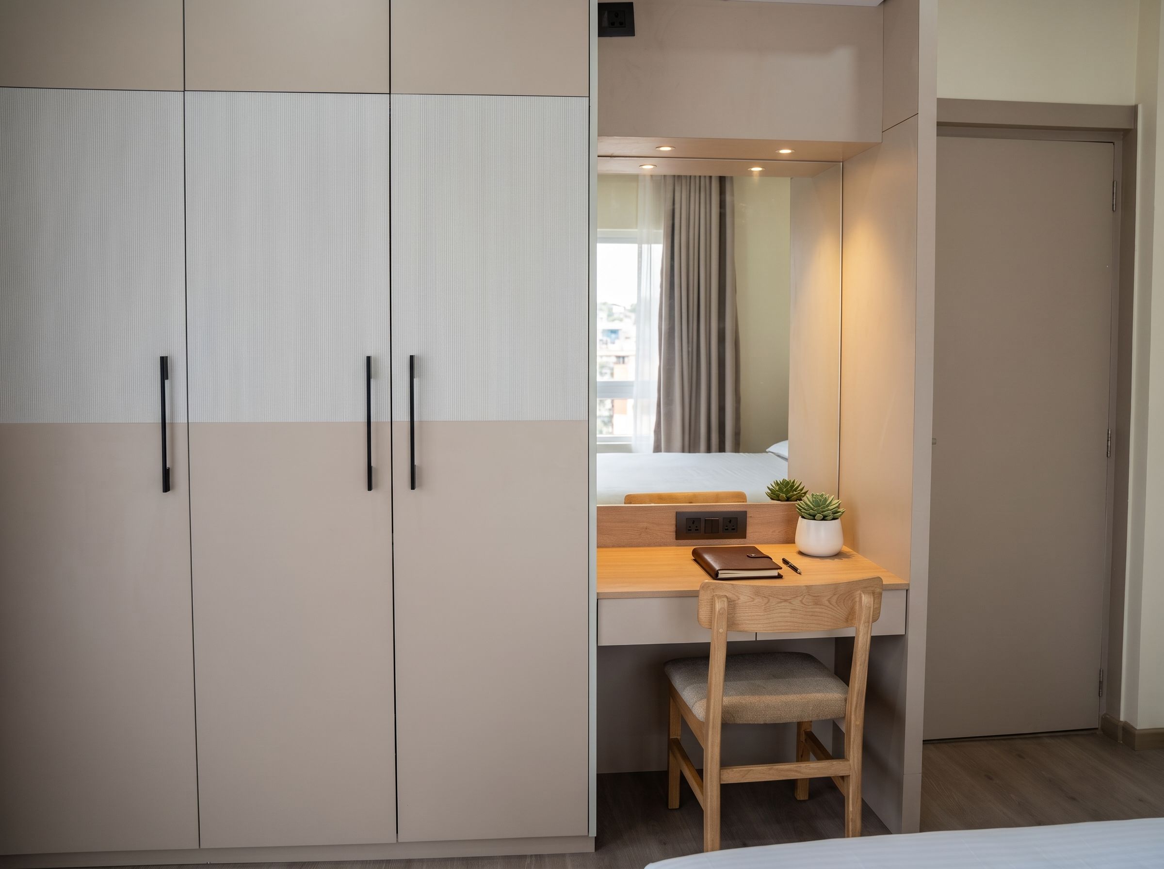 Een slaapkamer met een bed, een bureau met stoel, een kledingkast en een nachtkastje met een plant.