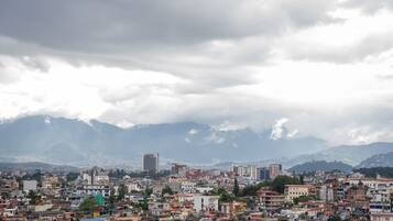 Un paisaje urbano con un edificio destacado en primer plano y montañas al fondo.