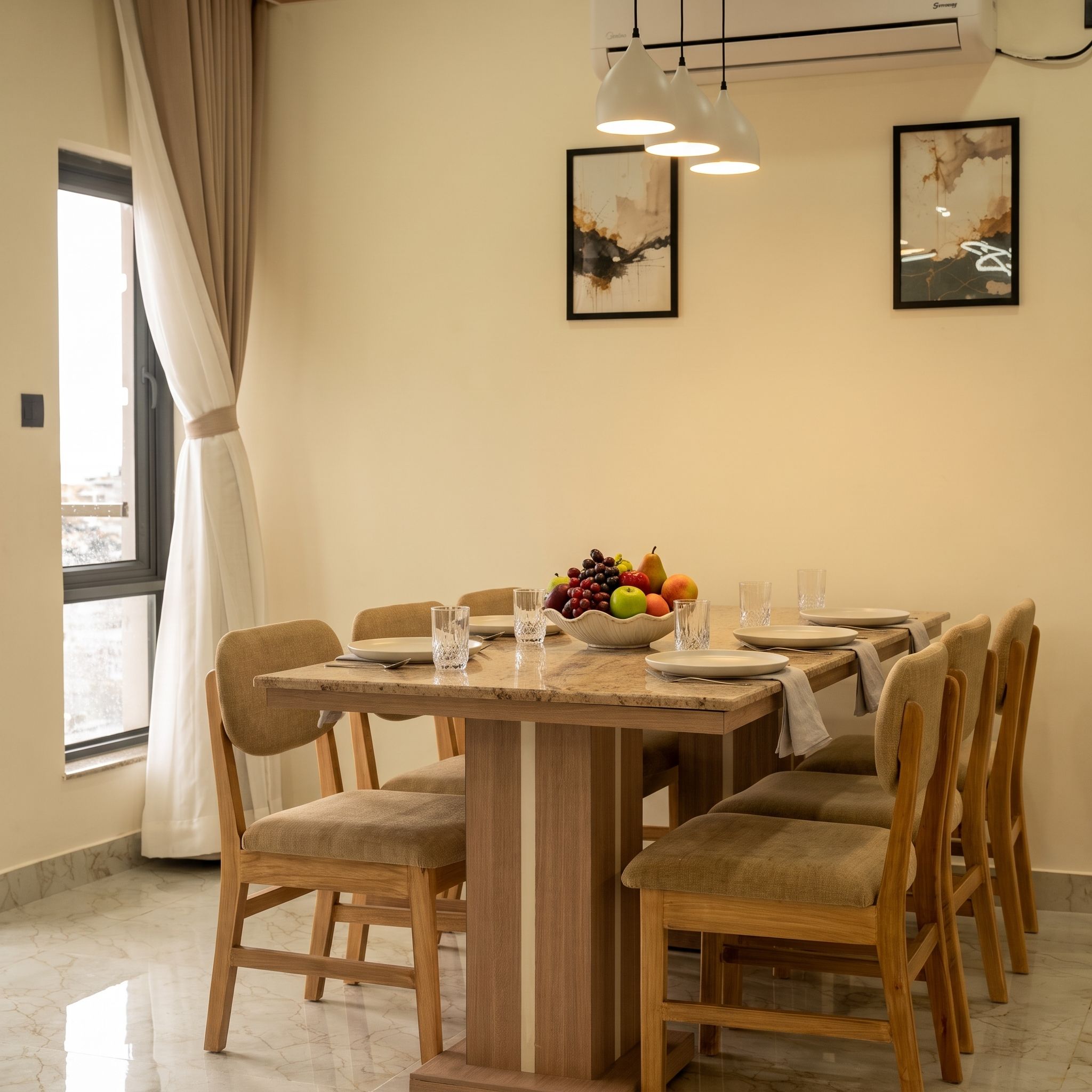 A dining area with a wooden table, chairs, a fruit bowl, and artwork on the wall.