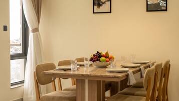 A dining area with a wooden table, chairs, a fruit bowl, and artwork on the wall.