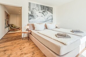 Ein Schlafzimmer mit einem großen Bett, einem Sessel, einem kleinen Tisch und einem Wandbild.