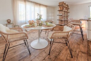 Ein Essbereich mit einem runden Tisch, Korbstühlen und einem Holzregal.
