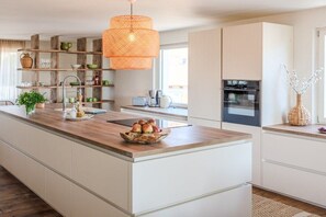 Cozinha moderna com ilha central, prateleiras de madeira e luminária pendente.