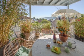 Eine Terrasse im Freien mit Korbmöbeln, einem Tisch gedeckt mit Weingläsern, einer Flasche und Topfpflanzen.