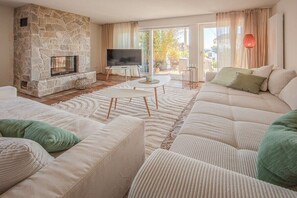 A living room with a stone fireplace, a flat-screen TV, and a sofa set. - Lake Apartment Panorama (Gaienhofen)