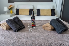 Ein ordentlich bezogenes Bett mit einer gemusterten Tagesdecke, zwei Handtüchern, einer Flasche und einem Glas in der Mitte.